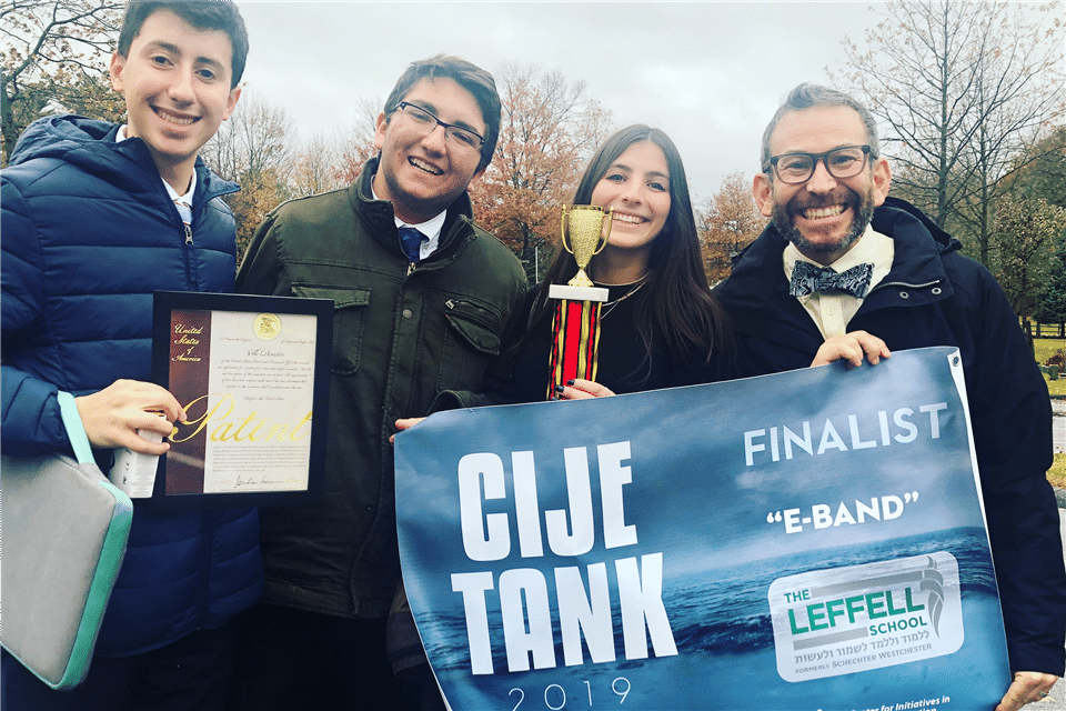 Three smiling individuals proudly hold a plaque together, celebrating their achievement.