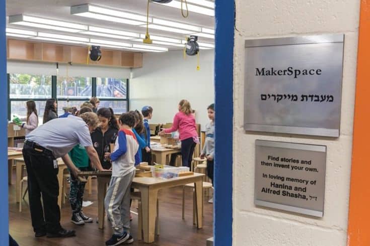 A group of people stands around a table in a classroom, engaged in discussion or collaborative work.