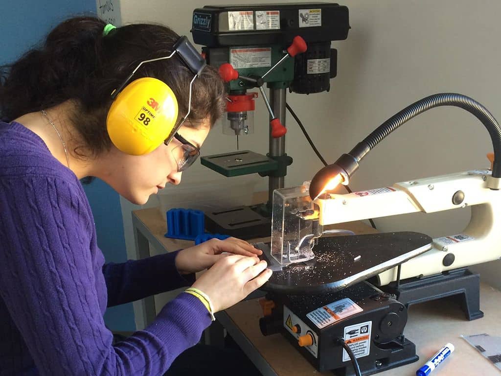 A woman wearing headphones operates a machine, focused on her task in a work environment.