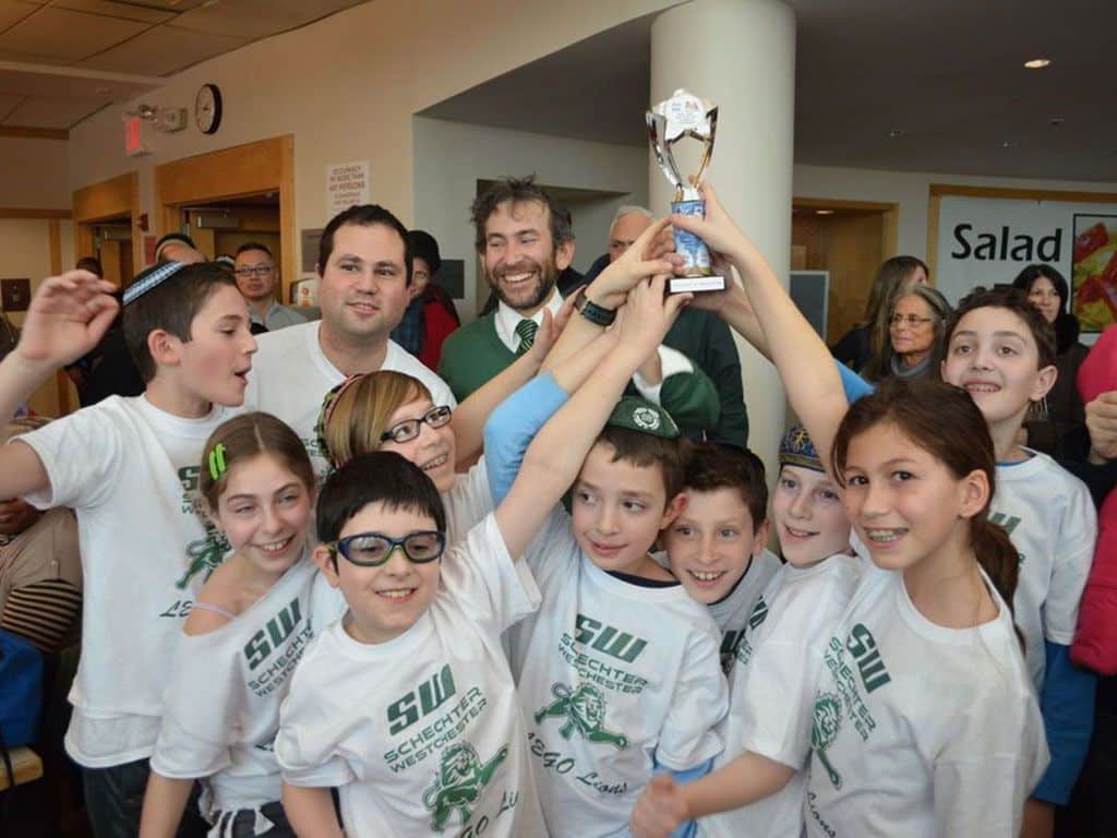 A group of smiling children proudly holding up a trophy together, celebrating their achievement.
