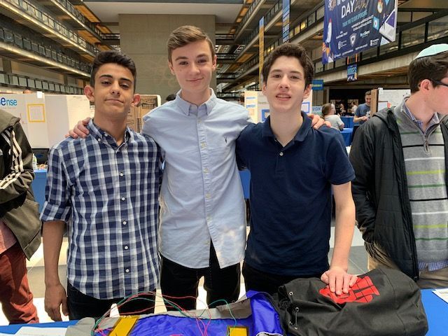 Three students behind a table smiling and posing for a picture