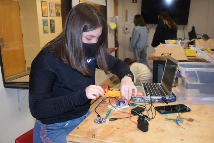 A girl is focused on assembling electronics components in a classroom setting.