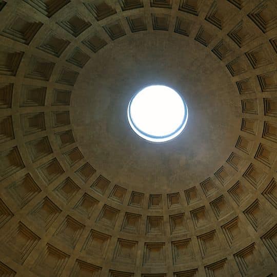 Inside view of a domed ceiling with a central circular opening, or oculus, surrounded by geometric patterns. The light creates a serene atmosphere.